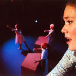 [Best Feature - Second] Maili Kee (10) from South High School performs "Millwork" in the dual-school musical, "Working," while Maggie Spicer (12) ballet dances in the presence of millworkers Courtney Tejral (12) and Haley Hrabe (12). The musical featured all-aged students from both of Salina's public high schools and a first-grade student from Stewart Elementary School. "Working" focused on inspiring students to pursue their true aspirations, and needed a very diverse cast to accommodate the substantial cast size. "This scene represented how many peoples' individuality is smothered by the monotone of particular jobs. Shortly after Maggie's dance performance, she resumes a position behind one of the desks to join the other millworkers," explained Kee. (Sarah Vanier, Salina Central High School, 5A, Salina, KS)