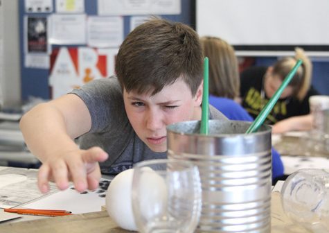 In an attempt to show the shadows and glares of the cans in a charcoal drawing, freshman Jack Jaworski reaches to adjust the staged cans and glasses during drawing on Wednesday, April 28.